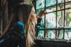 Woman looking out a broken window.