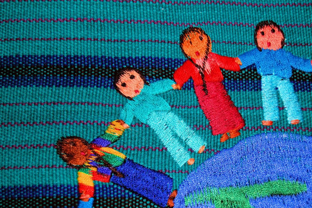 Sewn images of diverse people holding hands across a globe